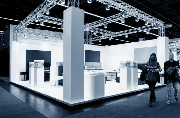 Stand de feria con estructura de truss iluminada y visitantes recorriendo el pabellón
