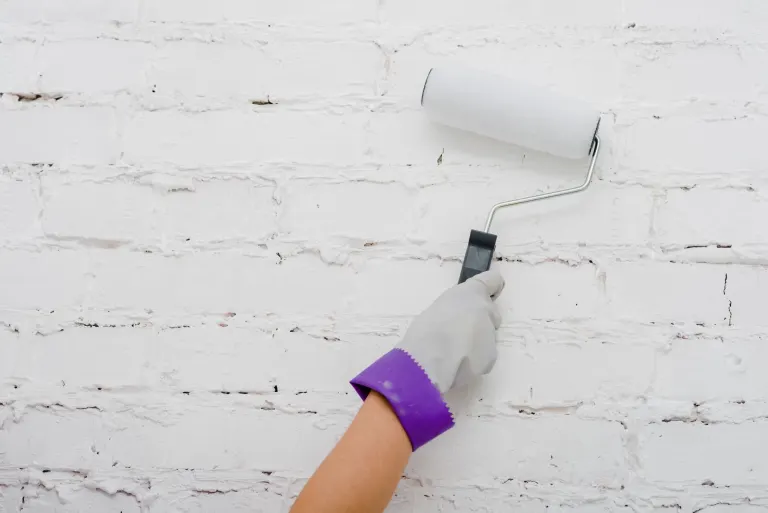 Mano pintando una pared de ladrillo con rodillo
