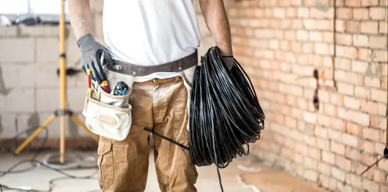 Electricista con herramientas y bobina de cable en obra